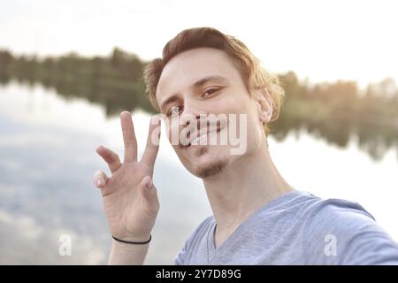 Porträt des jungen, hübschen, lächelnden Mannes, der Selfie gegen den See macht. Wunderschöne Natur Stockfoto