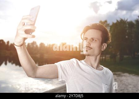 Porträt des jungen, hübschen, stylischen lächelnden Mannes, der Selfie am Strand macht. Wunderschöne Natur Stockfoto