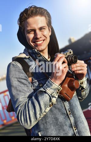 Stilvoller Mann, der mit einer Retro-Kamera fotografiert. Touristen bleiben auf der Brücke und machen ein Foto Stockfoto