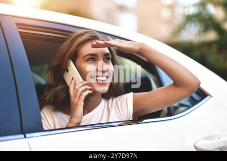 Schöne Frau mit lächelndem Telefon, während sie auf dem Rücksitz im Auto sitzt Stockfoto