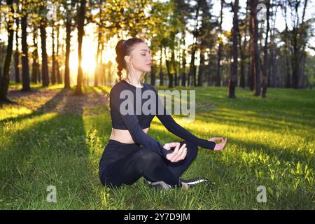 Eine Frau meditiert in einem Wald bei Sonnenuntergang, engagiert sich in Yoga und Achtsamkeit, umgeben von der Schönheit der Natur Stockfoto