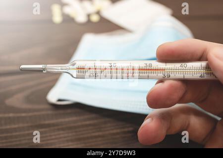 Ein medizinisches klinisches Quecksilberthermometer in der Hand, das die Temperatur von 39 C anzeigt. Hohe Temperatur. holzhintergrund. Thema Gesundheitswesen, ich Stockfoto