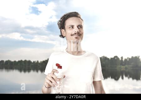 Der Junge trinkt frisches Wasser vor dem See und dem Waldgrund. Sommerdurst. Wunderschöne Aussicht Stockfoto