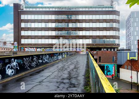 Eine urbane Szene mit einem großen Bürogebäude mit Graffiti-bedeckten Wänden und einem leeren, nassen Pfad, der zu ihm führt Stockfoto