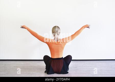 Rückansicht einer charmanten blonden Ballerina sitzt auf dem Boden im Ballsaal, der sich vor der Vorstellung aufwärmt Stockfoto