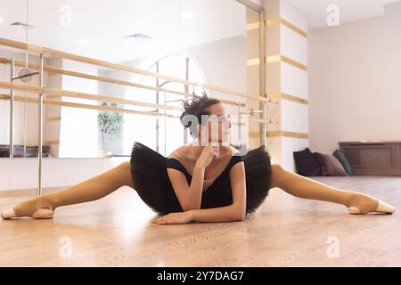 Eine Ballerina in schwarzem Tutu und spitzenschuhen dehnt sich auf dem Boden in einem Ballettstudio Stockfoto