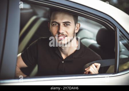 Ein junger, gutaussehender Mann schnallt den Sicherheitsgurt an, sitzt auf dem Rücksitz des Autos Stockfoto