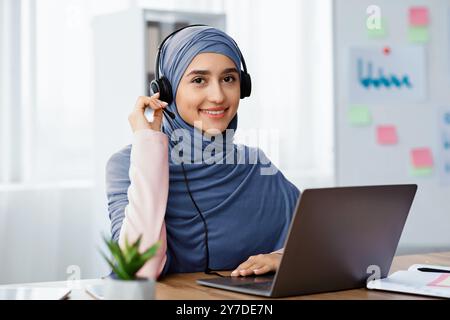 Schöne arabische Frau im Hijab, die ein Headset trägt, das in modernen Büros arbeitet Stockfoto