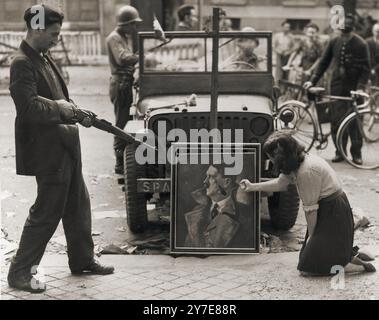 Ein französischer Zivilist und ein französischer Widerstandskämpfer enttarnen kurz nach der Befreiung ein Porträt Adolf Hitlers in Paris. Stockfoto