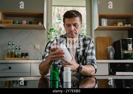 Der Mann sitzt am Tisch in der Küche und sieht sich verschiedene Flaschen mit Medikamenten-Kapseln an. Die Person nimmt Pillen oder Vitamine ein. Das Konzept der Nahrungsergänzungsmittel, medici Stockfoto