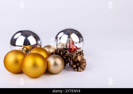 Tannenzapfen sind wunderschön dekoriert mit leuchtend roten Glocken und goldensilbernen Weihnachtsschmuck in verschiedenen Größen, vor einem sauberen weißen Hintergrund Stockfoto