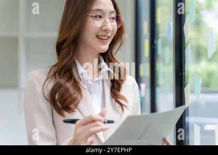 Glückliche junge Geschäftsfrau, die allein im Büro an ihrem Projekt arbeitet Stockfoto