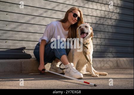 Eine blinde Frau geht mit ihrem Blindenhund auf die Straße. Ein Mädchen, das einen labrador umarmt. Stockfoto