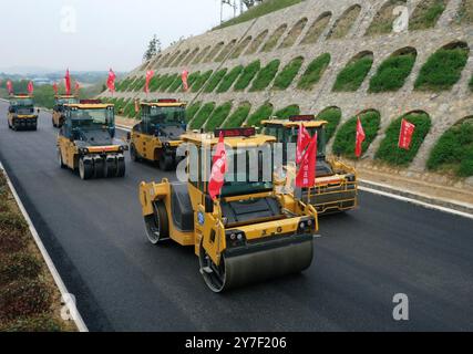 (240930) -- ZHENGZHOU, 30. September 2024 (Xinhua) -- Ein Drohnenfoto zeigt unbemannte Straßenwalzen, die an einem Abschnitt einer Schnellstraße entlang des Dabie-Gebirges in der zentralchinesischen Provinz Henan arbeiten, 11. April 2024. Henan liegt strategisch im zentralen Teil des Landes und ist seit Jahrhunderten ein nationaler Verkehrsknotenpunkt. In den vergangenen Jahrzehnten baute die Provinz ein modernes Verkehrsnetz aus Flugzeugen, Eisenbahnen, Autobahnen, Wasserkanälen und allen möglichen Häfen. Sie weitet ihre Rolle nun rasch auf Bereiche der grenzüberschreitenden Logistik, Investitionen und des Handels aus, um sie zu erleichtern Stockfoto