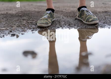Eine Person steht in einer Wasserpfütze mit den Füßen im Wasser. Die Reflexion der Person ist im Wasser sichtbar Stockfoto