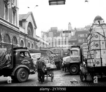 Ein Teil des Covent Garden Market mit Trucks, die hoch gestapelt sind mit Obst- und Gemüseboxen und einem Portier, der einen Handwagen zieht. An Drähten oben ist die Streifenbeleuchtung zu sehen, die den Markt in den frühen Morgenstunden beleuchtet, wenn die Arbeit in der Gegend am meisten beschäftigt ist. - 9. Dezember 1960 Stockfoto