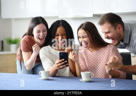 Begeisterte Freunde feiern Erfolg beim Telefonieren in der Küche zu Hause Stockfoto