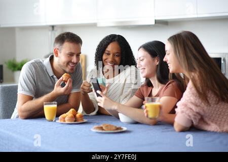 Glückliche Freunde, die beim Frühstück in der Küche zu Hause telefonieren Stockfoto