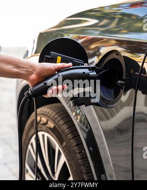 Nahaufnahme des Handsteckens des EV-Ladegeräts in das Elektrofahrzeug draußen. Stockfoto