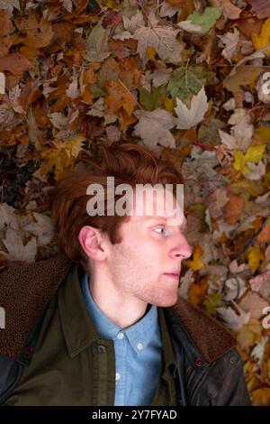 Ein junger Mann ruht auf einem lebhaften Teppich aus herbstlichen Blättern Stockfoto