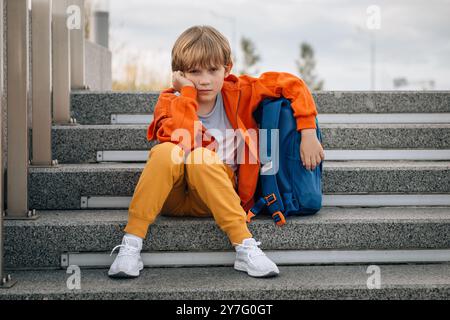 Kleiner Junge, Schuljunge, mit Rucksack sitzt auf der Treppe und ist traurig Stockfoto