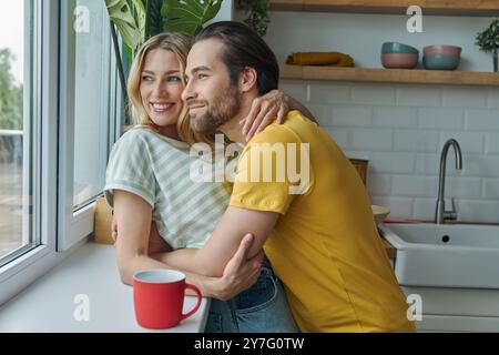 Wunderschönes junges Paar, das durch ein Fenster schaut, während er in der Küche steht Stockfoto