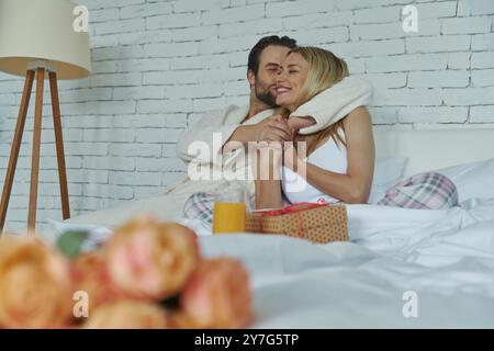 Wunderschönes Paar, das sich im Bett umschließt, während ein Haufen Rosen im Vordergrund liegt Stockfoto