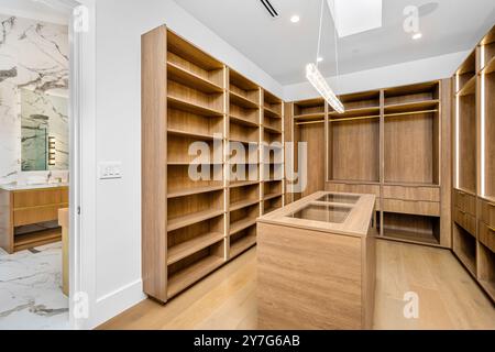 Ein moderner begehbarer Kleiderschrank mit Holzregalen und einer Insel mit Glasdach, neben einem Marmorbad. Stockfoto