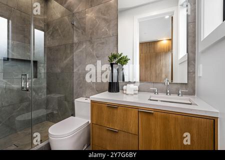 Modernes Bad mit Holzwaschtisch, Glasdusche und grauen gefliesten Wänden, elegantem Design und moderner Einrichtung. Stockfoto