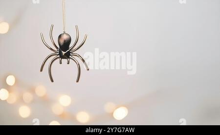 Halloween-Thema schwarz-goldene Kunststoff-Kunstspinne, die von Goldfaden mit verschwommenen Bokeh-Lichtern auf einem neutralen hellbraunen Hintergrund mit Spac hängt Stockfoto