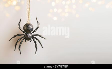 Halloween-Thema schwarz-goldene Kunststoff-Kunstspinne, die von Goldfaden mit verschwommenen Bokeh-Lichtern auf einem neutralen hellbraunen Hintergrund mit Spac hängt Stockfoto