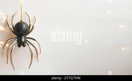 Halloween-Thema schwarz-goldene Kunststoff-Kunstspinne, die von Goldfaden mit verschwommenen Bokeh-Lichtern auf einem neutralen hellbraunen Hintergrund mit Spac hängt Stockfoto