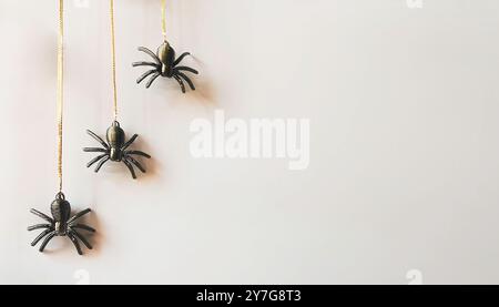 Gruselige Halloween kleine schwarze Kunstplastik Spinnendekorationen hängen von Goldfäden isoliert vor einem hellen cremeweißen, neutralen Hintergrund. Stockfoto