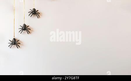 Gruselige Halloween kleine schwarze Kunstplastik Spinnendekorationen hängen von Goldfäden isoliert vor einem hellen cremeweißen, neutralen Hintergrund. Stockfoto