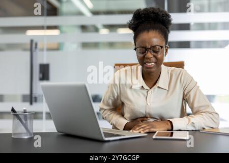 Geschäftsfrau im Büro, die Beschwerden hat. Sitzen am Schreibtisch mit Laptop und Telefon, halten den Magen, zeigen arbeitsbedingten Stress oder gesundheitliche Probleme während des Arbeitstages. Stockfoto
