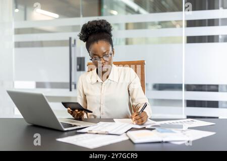 Finanzbuchhalter im modernen Bürorechner, der sich mit Papierkram beschäftigt und sich auf Finanzanalysen konzentriert. Der Arbeitsplatz verfügt über Laptops und Dokumente, die auf professionelles Multitasking hinweisen Stockfoto