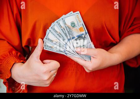 Eine Frau in einer roten Bluse hält Geld mit einem Ventilator und gibt den Daumen hoch Stockfoto