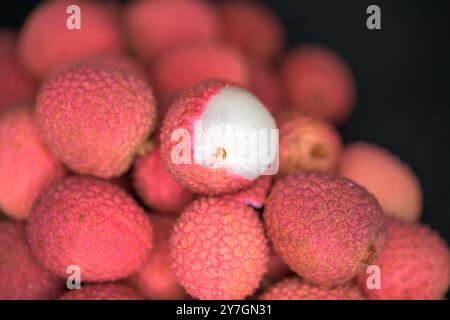 Eine Nahaufnahme reifer Litschis, die sich aneinanderstapeln, wobei eine geöffnete Frucht ihr saftiges weißes Fleisch zeigt Stockfoto