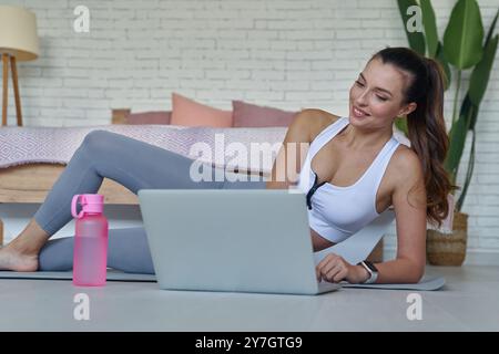 Schöne junge Frau in Sportbekleidung, die vor dem Training zu Hause Online-Unterricht ansieht Stockfoto