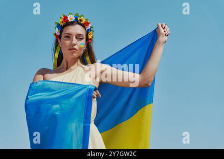 Junge ukrainische Frau mit Nationalflagge und Blick in die Kamera mit Himmel im Hintergrund Stockfoto