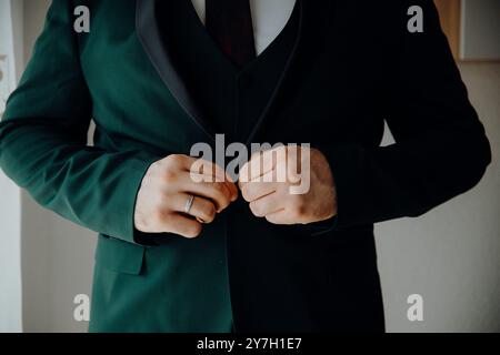 Nahaufnahme eines Mannes in einem dunklen Anzug, der seine Jacke anpasst, sich auf Hände und Ehering konzentriert. Stockfoto