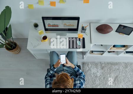 Draufsicht eines Mannes, der sein Smartphone hält, während er an seinem Arbeitsplatz sitzt Stockfoto