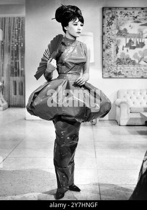 13. MAI 1964 gleitende Schönheit. Shirley MacLaine sieht ein bisschen träumerisch aus, wo Edith Head seine einzigartige Kreation in einer Szene aus „What a Way to Go“ hat. Das Kleid ist wahrscheinlich das einzige Lederkostüm der Welt. Es musste mit flüssigem Zement zusammengesetzt werden, direkt auf dem Stern. Der extrem schlanke Rock ist so eng, dass man sich in ihm bewegen muss. In hellstem Chinesisch-Rot, das Kleid als neuartiger Pilzpouff se Pflaume an den Hüften. Hollywood, Kalifornien, USA Stockfoto