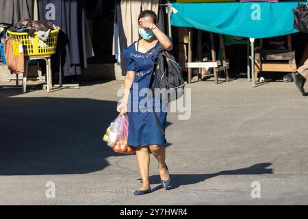 Frau geht die Straße runter und versteckt ihr Gesicht vor der Sonne Stockfoto