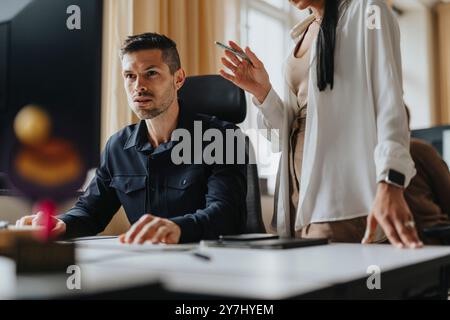 Konzentrierter Geschäftsmann, der am Desktop-PC arbeitet, sitzt in der Nähe von weiblichen Kollegen im Büro Stockfoto