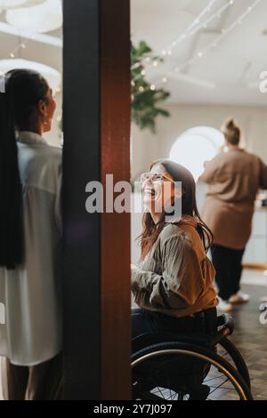 Glückliche junge Geschäftsfrau mit körperlicher Behinderung, die auf dem Rollstuhl sitzt und mit der Kollegin im Büro diskutiert Stockfoto