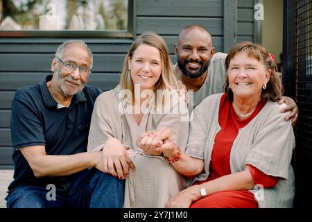 Porträt einer glücklichen Mehrgenerationsfamilie, die Hände hält, während sie auf der Veranda sitzt Stockfoto