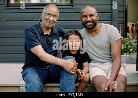 Porträt eines lächelnden Jungen, der mit Vater und Großvater auf der Veranda sitzt Stockfoto