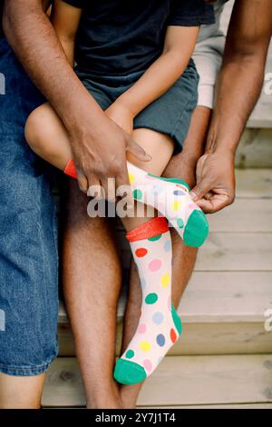 Hände des Vaters, der dem Sohn hilft, während er bunte Socken trägt Stockfoto