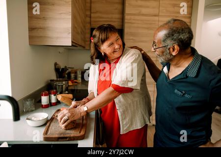 Seniorenmann mit Hand auf Schulter einer Frau, die zu Hause Essen in der Küche zubereitete Stockfoto